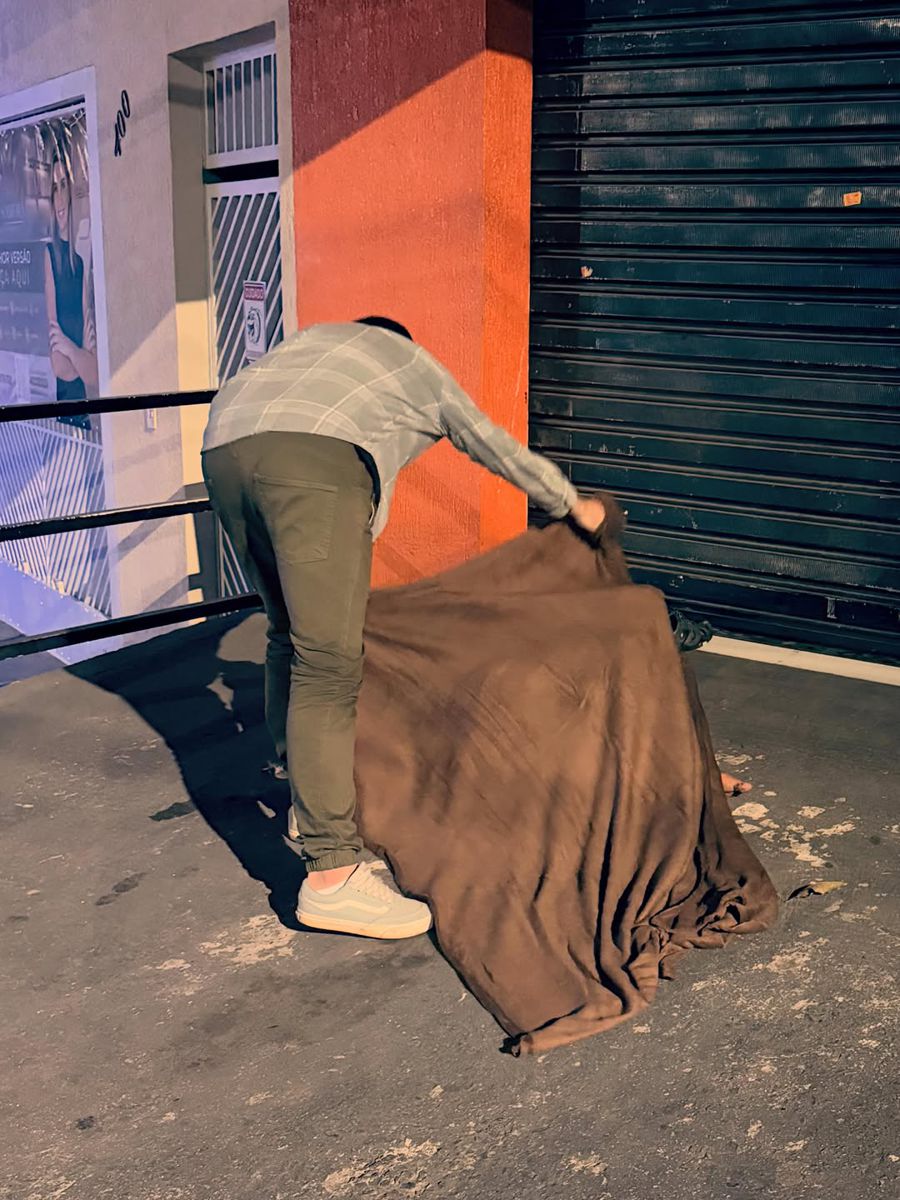 Voluntária cobrindo pessoa em situação de rua com cobertor durante a noite