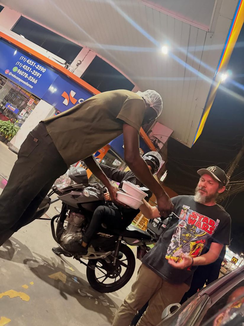 Voluntário conversando e entregando comida a pessoa com carrinho