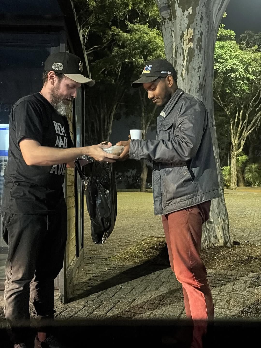 Voluntário do Bem da Madrugada entrega chocolate quente e comida a um homem durante ação noturna em Cotia